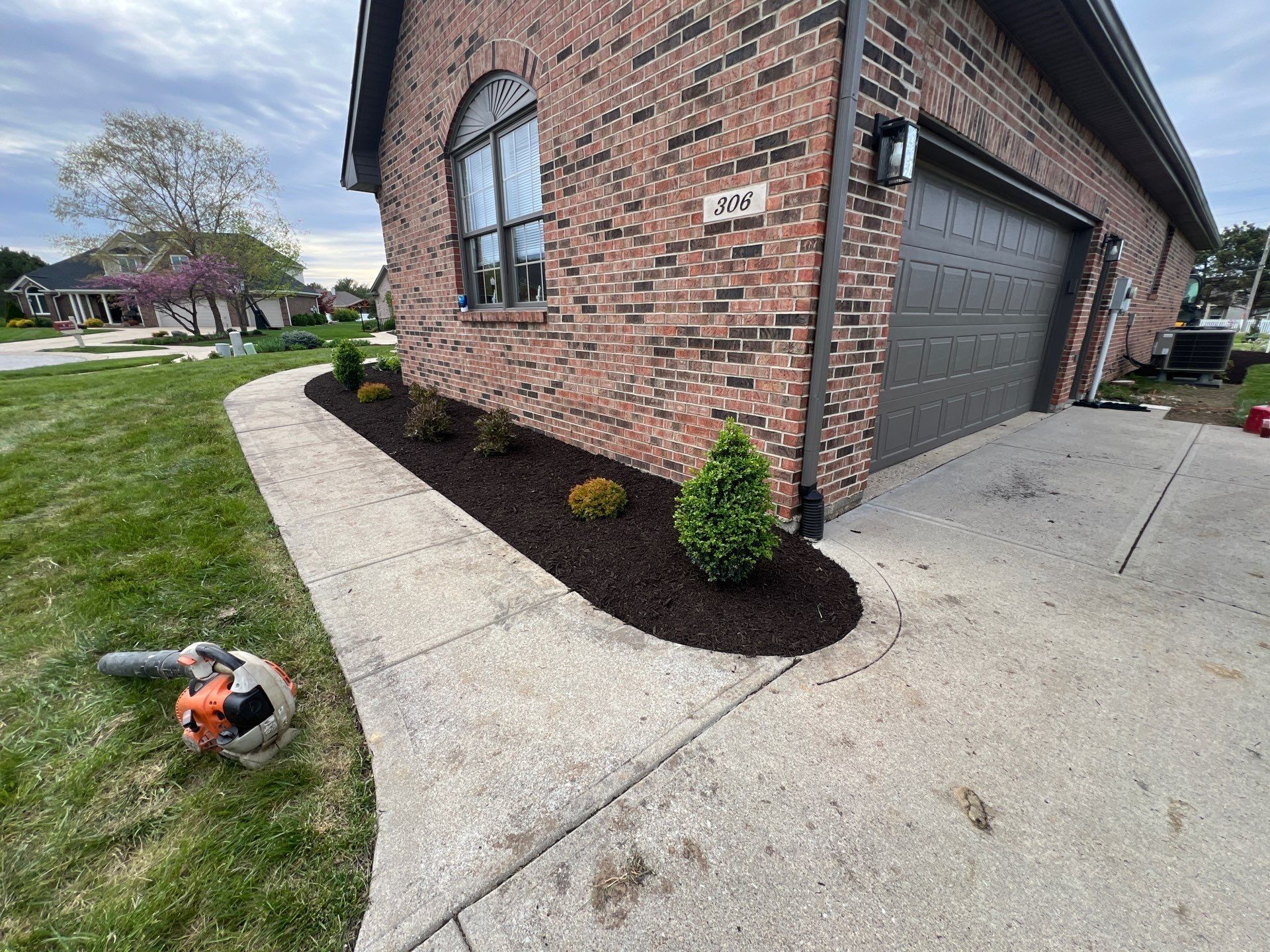 A lawn mower is sitting on the sidewalk in front of a brick house.