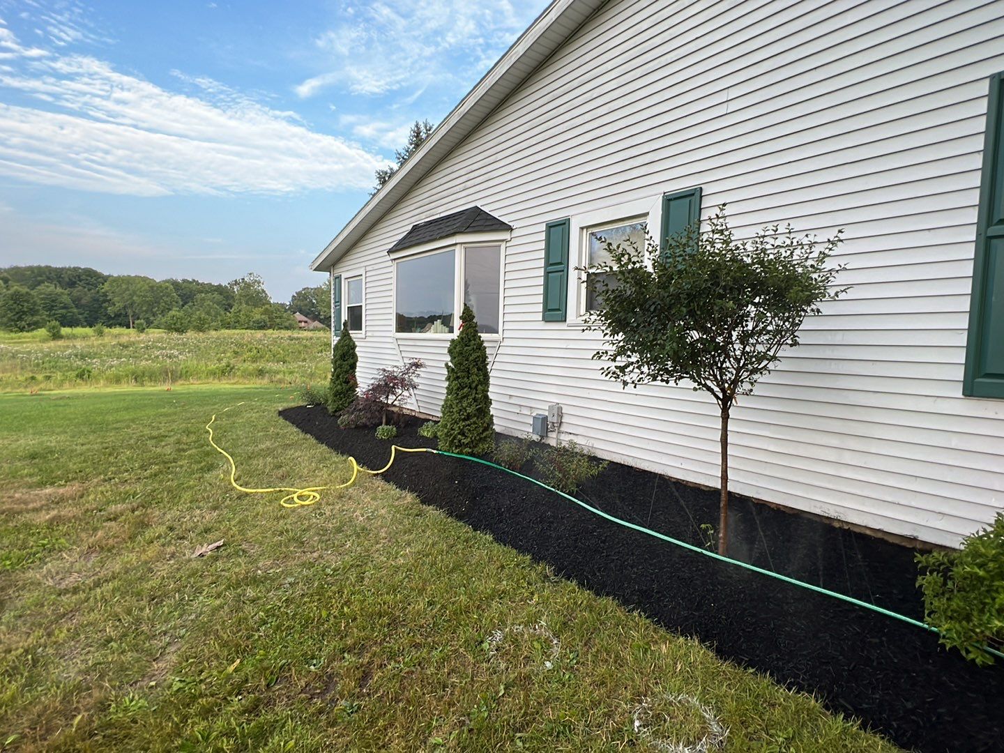 A white house with green shutters and a hose in front of it