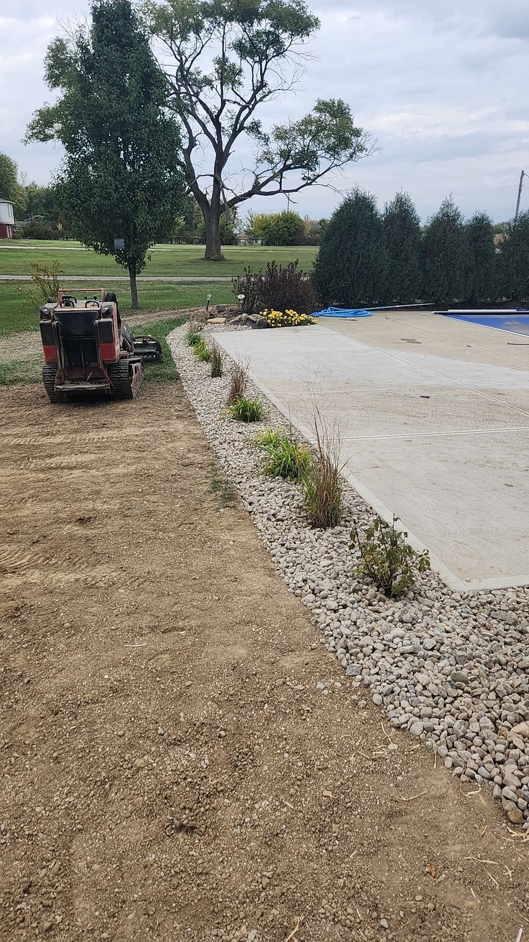 A tractor is sitting in the dirt next to a swimming pool.