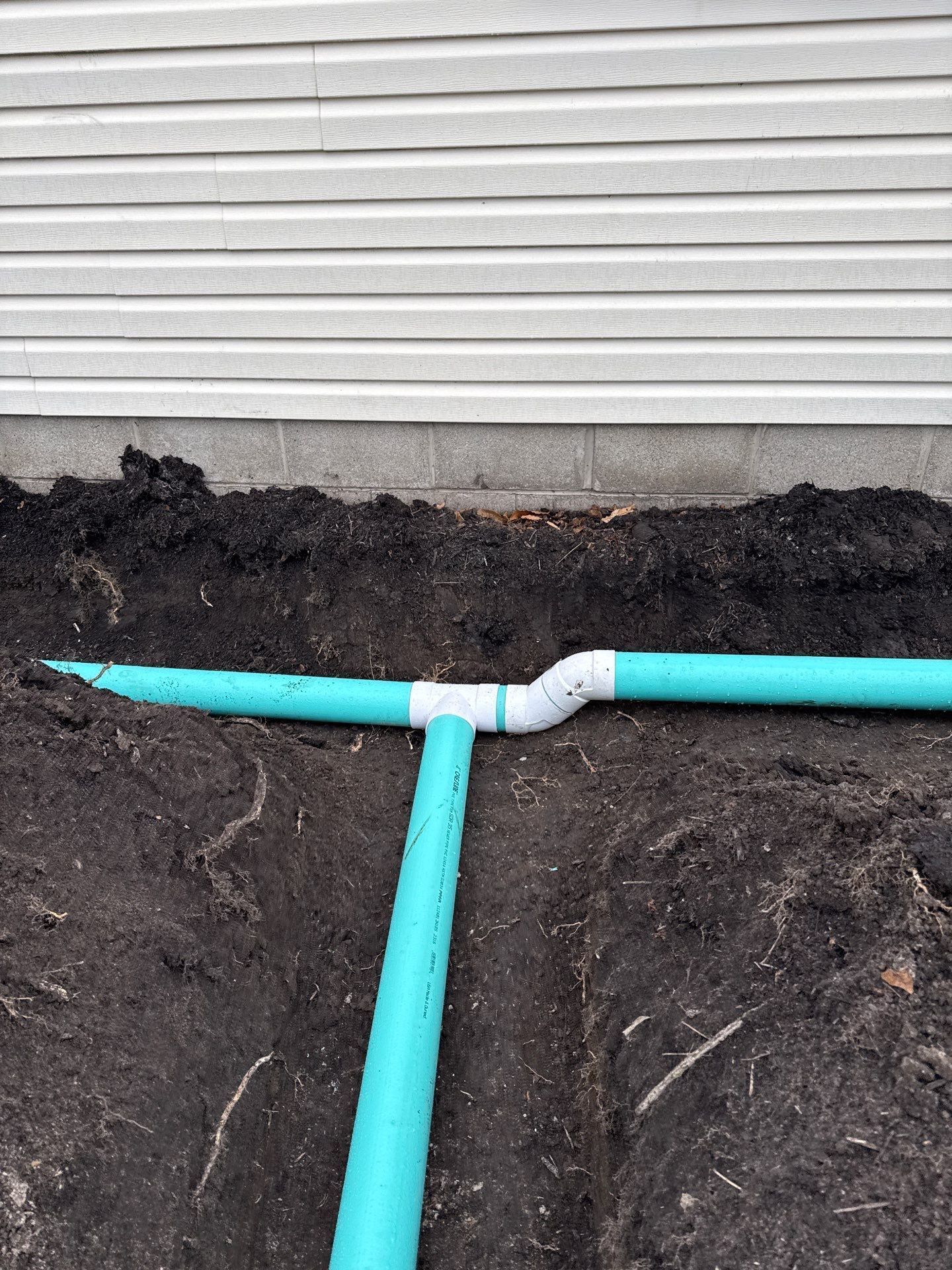A drain pipe is being installed in the dirt in front of a house.