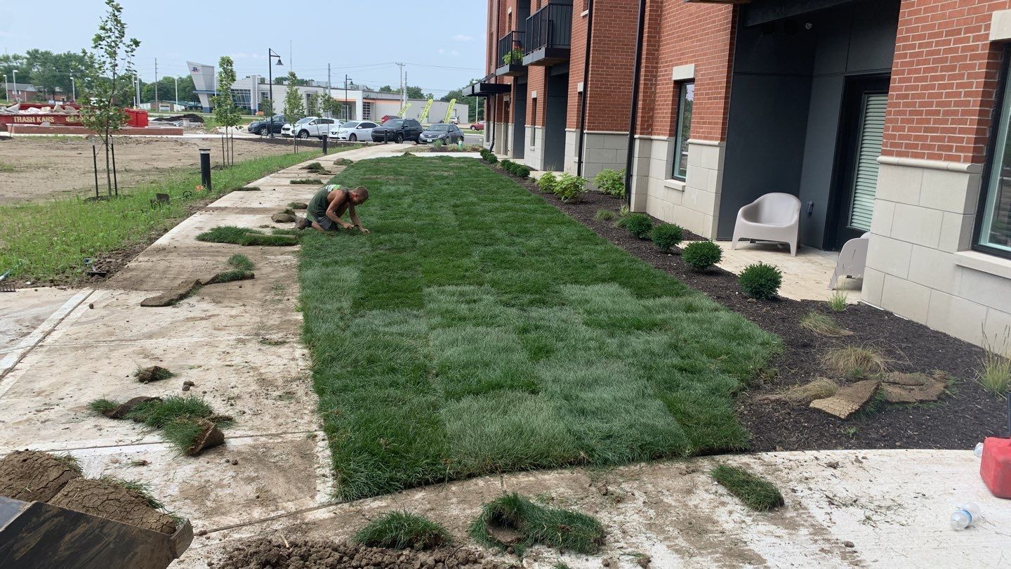 A man is working on a lawn in front of a brick building.