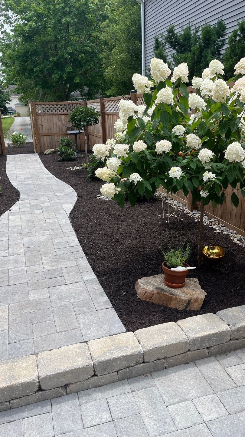 A walkway leading to a house with flowers and a fence.