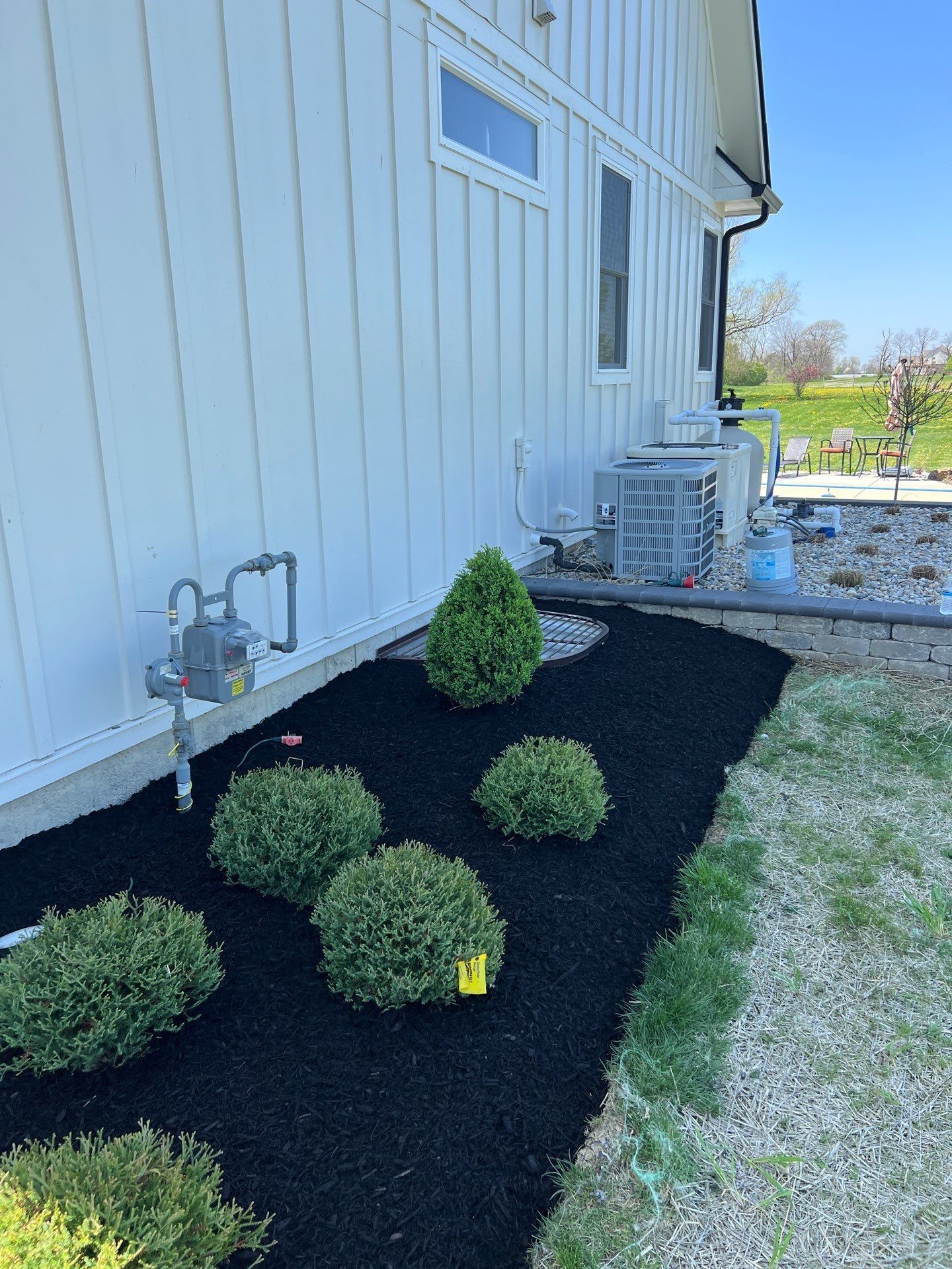 A white house with black mulch and bushes in front of it.