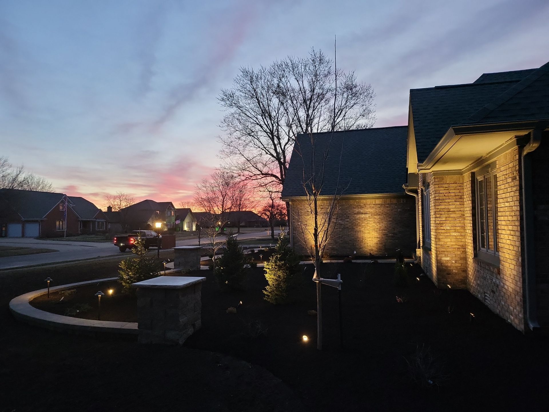 A brick house is lit up at night with a sunset in the background.