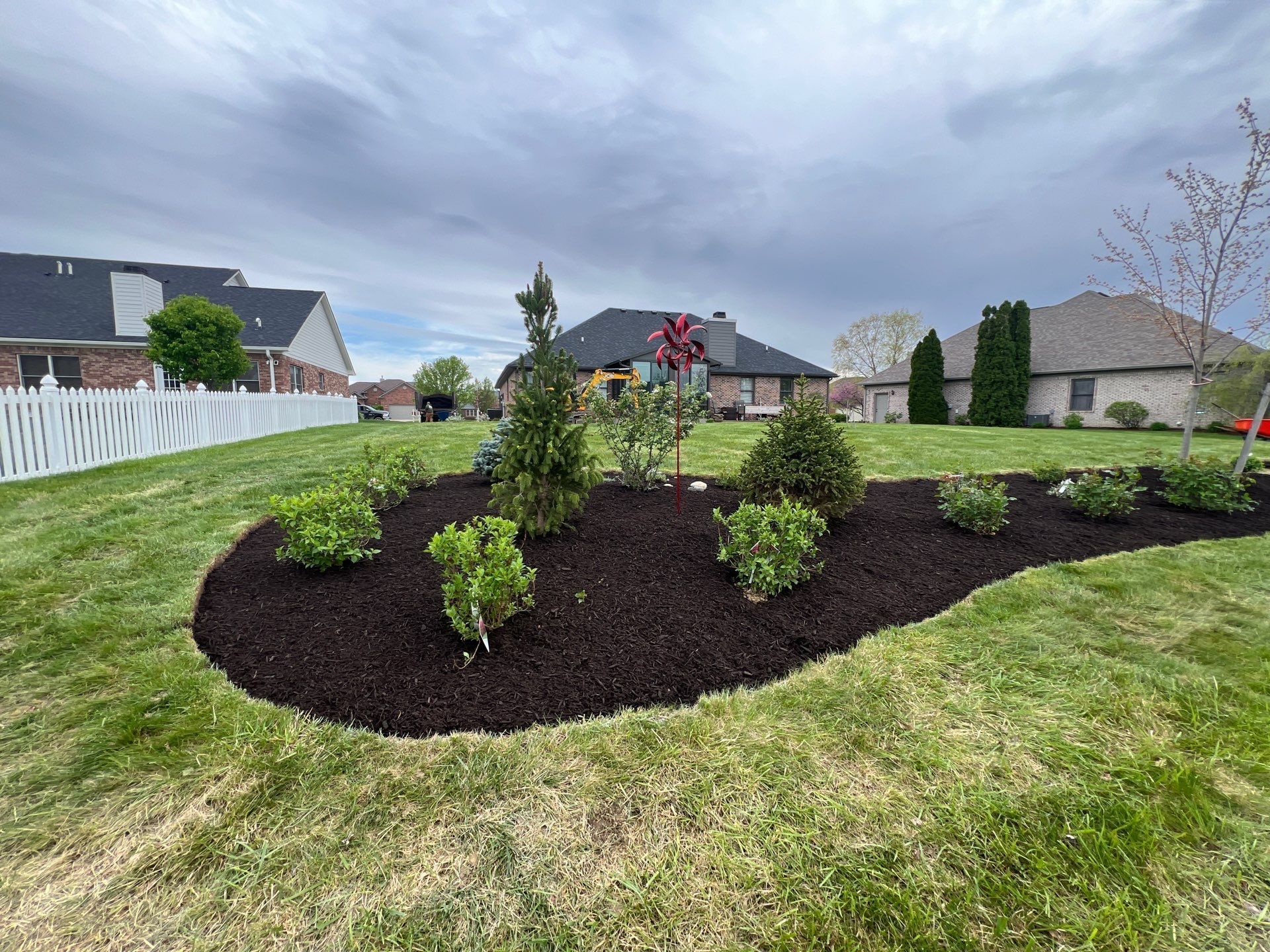 A lush green lawn with a white fence and a bush in the middle of it.