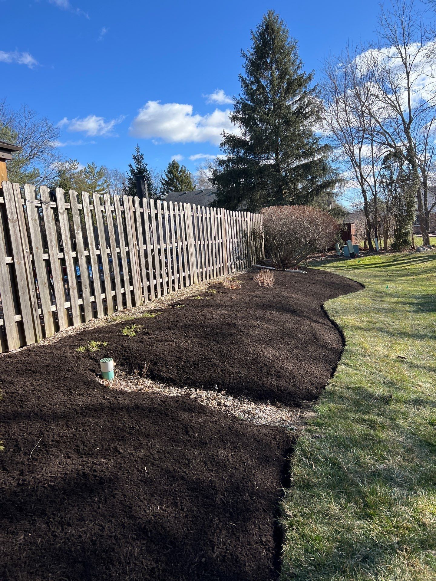A wooden fence is surrounded by black mulch in a yard.