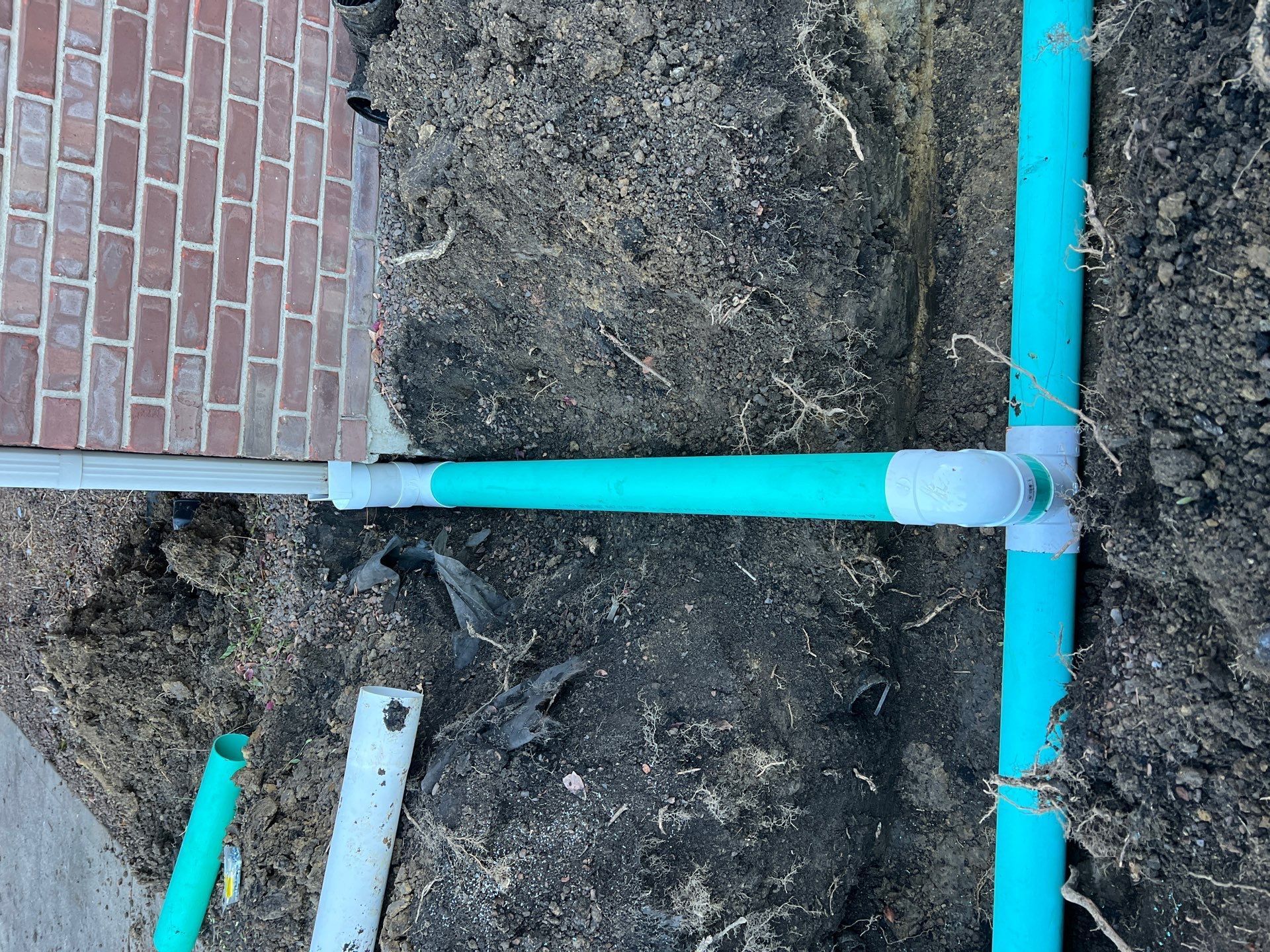 A green pipe is laying in the dirt next to a brick wall.