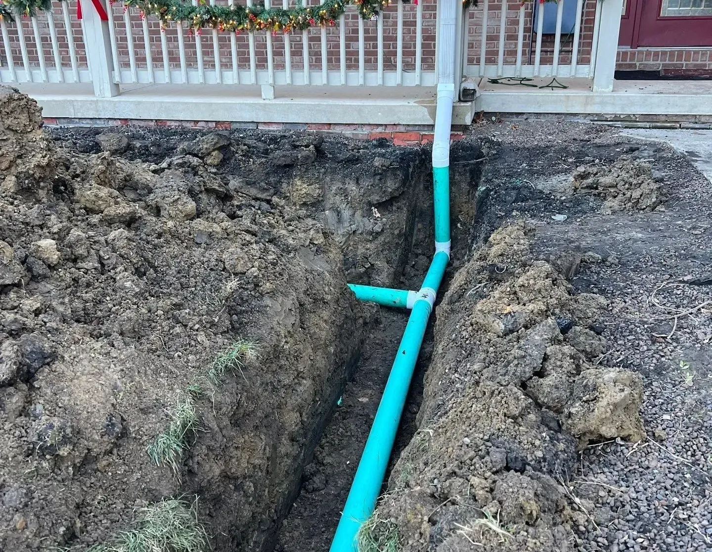 A trench dug in front of a house with green drainage pipes installed.