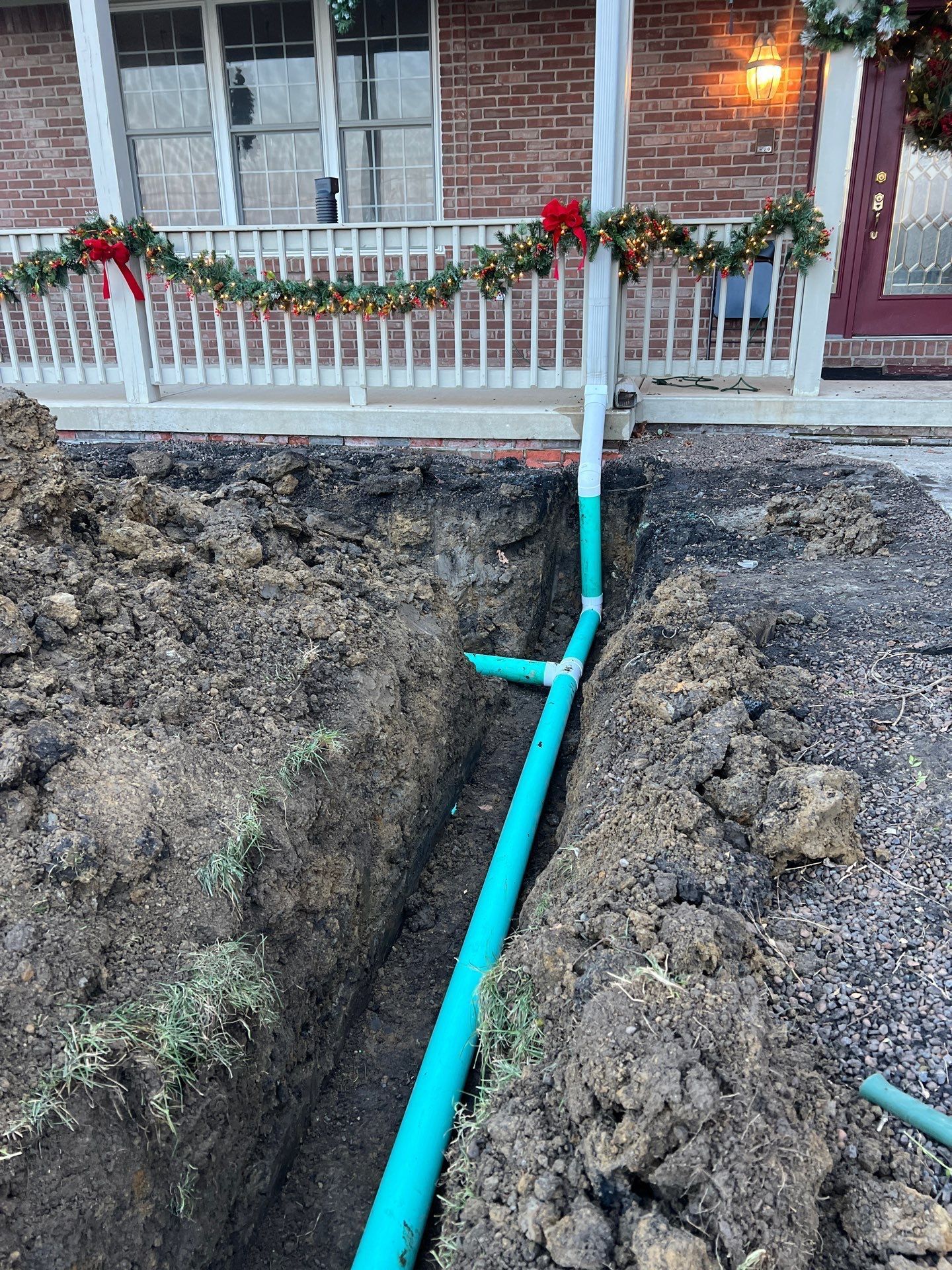 A green pipe is being installed in the dirt in front of a house.