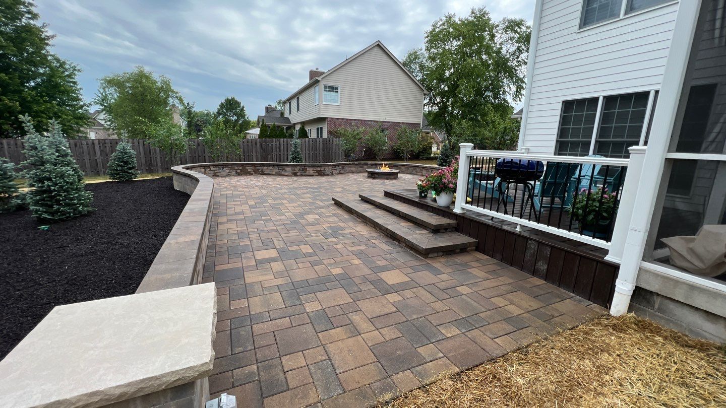 A patio with steps leading up to a deck and a house in the background.