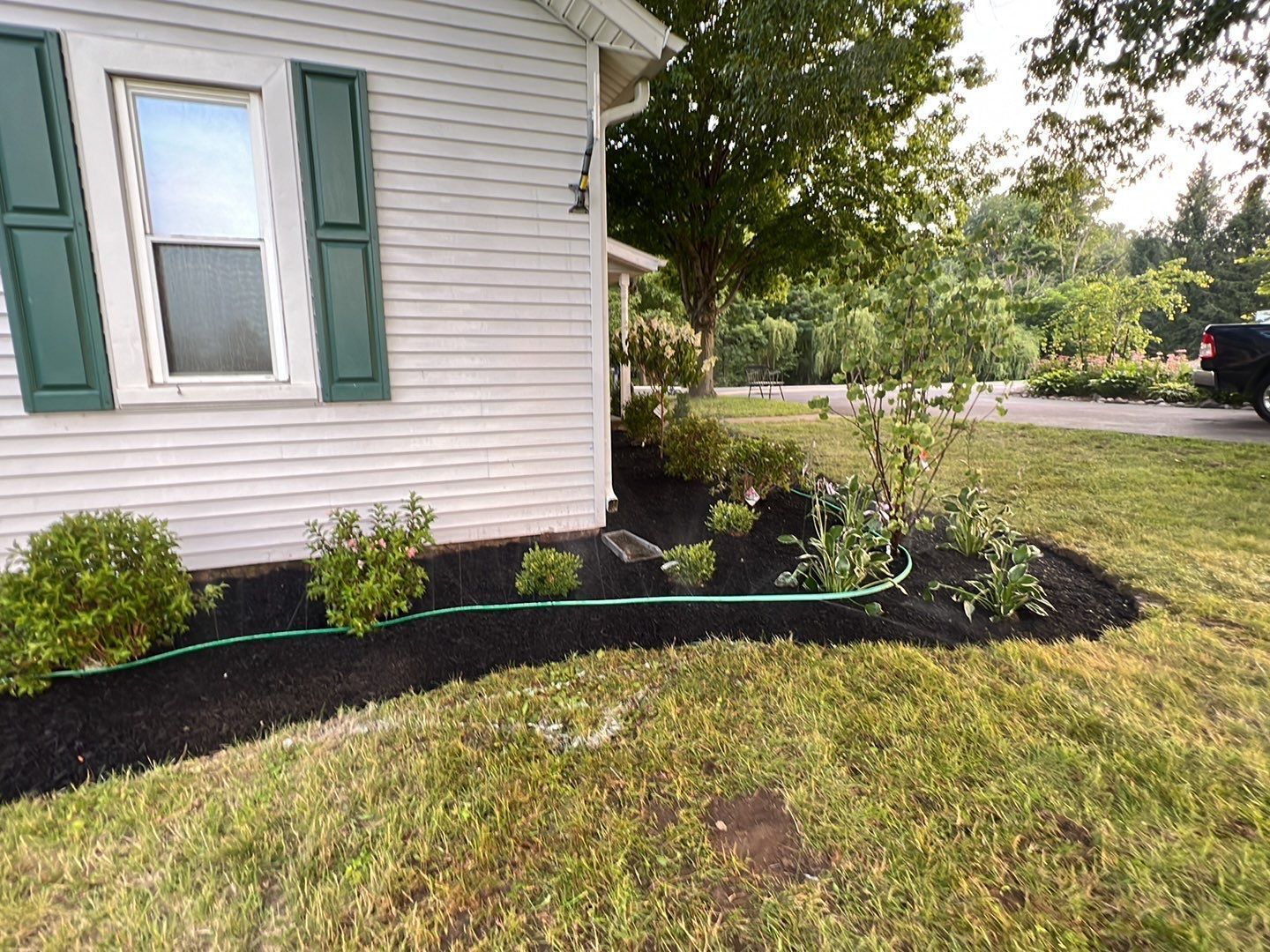 A white house with green shutters and a hose in front of it.