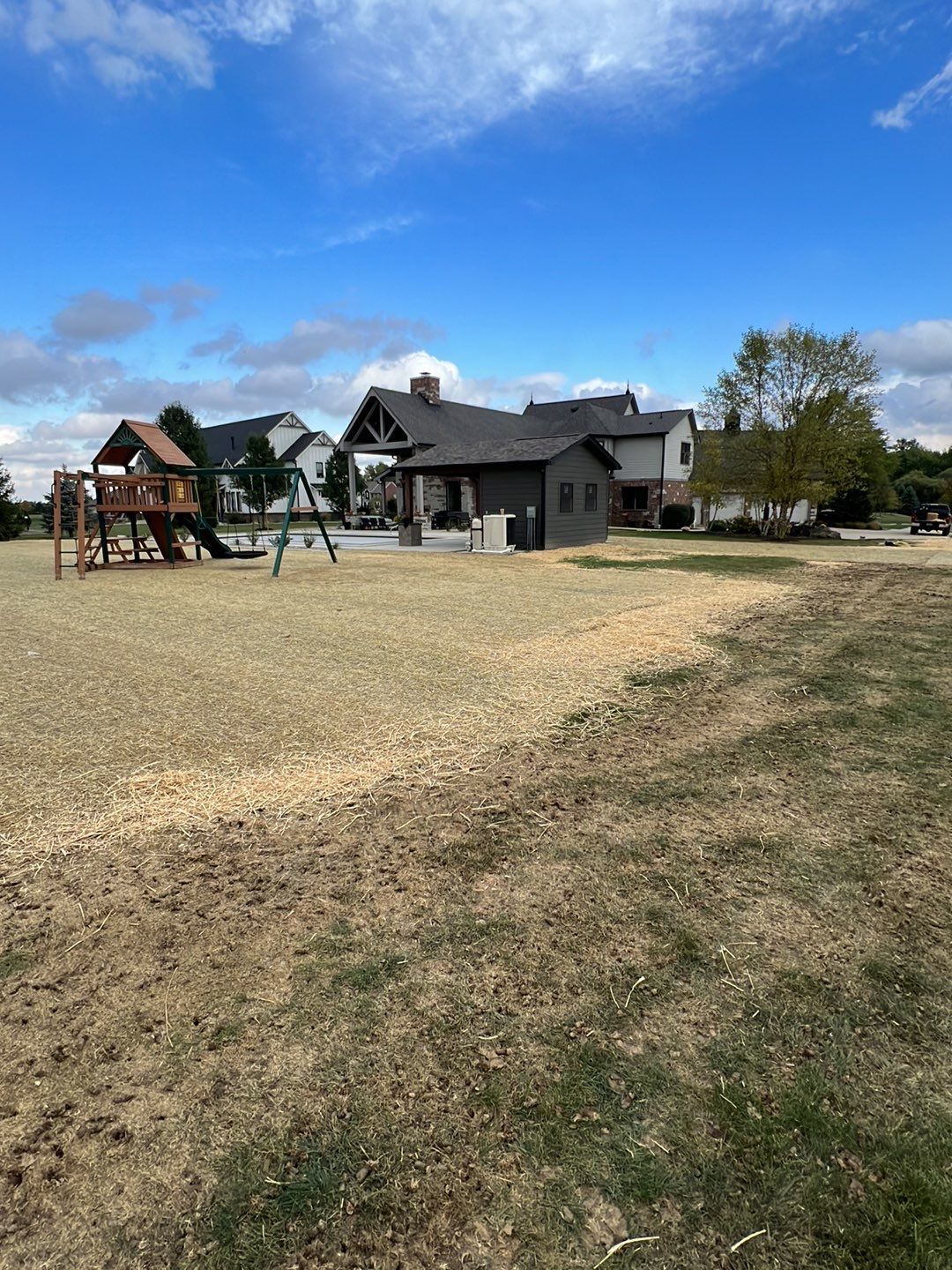 There is a playground in the middle of a field with a house in the background.