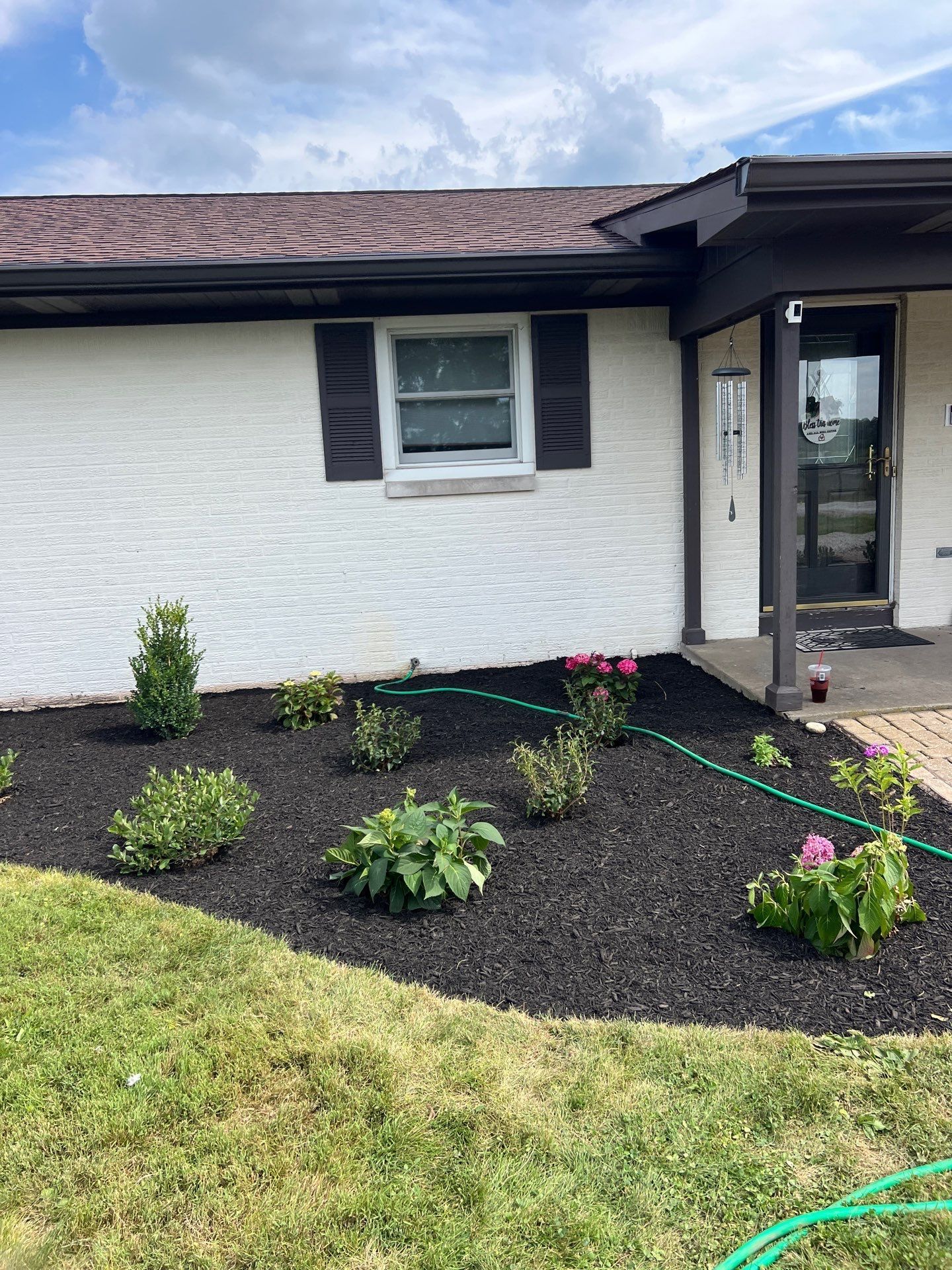 A white house with black shutters and a hose in front of it.