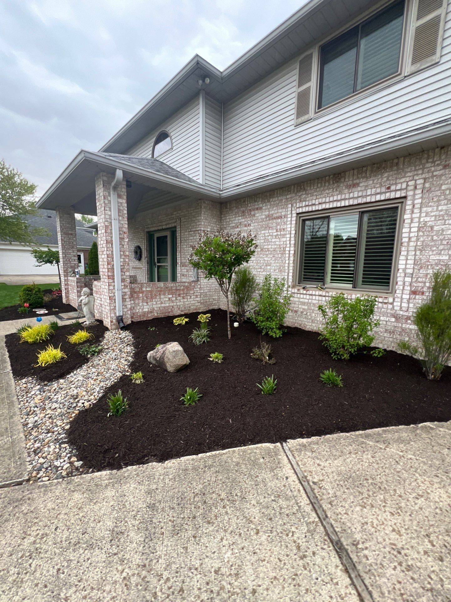 A large white brick house with a lush green garden in front of it.