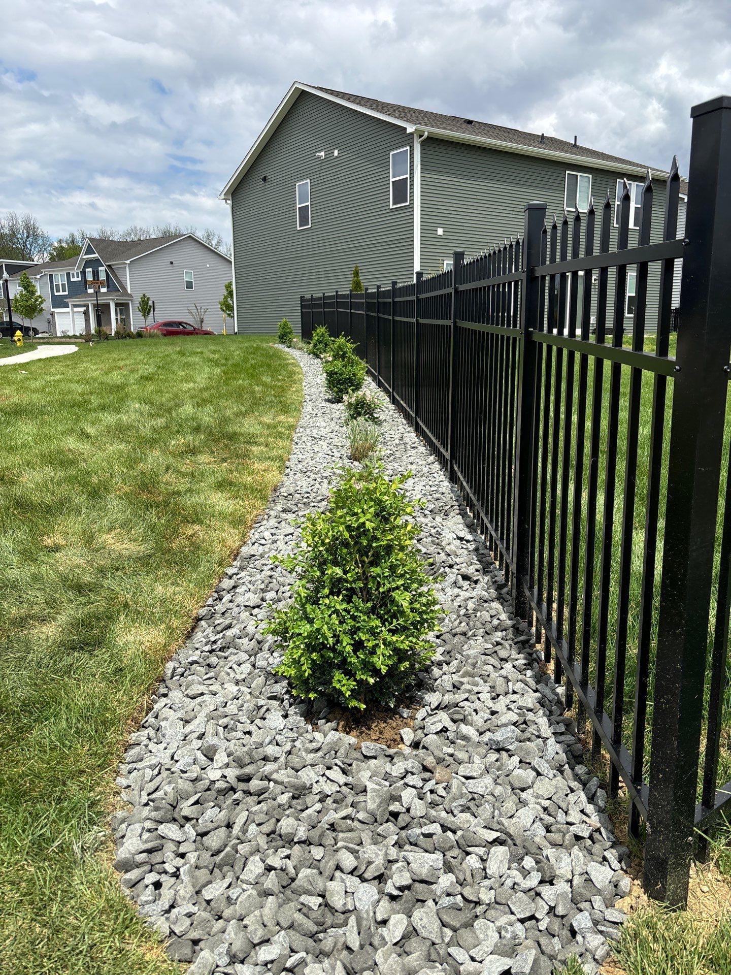 A black fence surrounds a gravel path leading to a house.