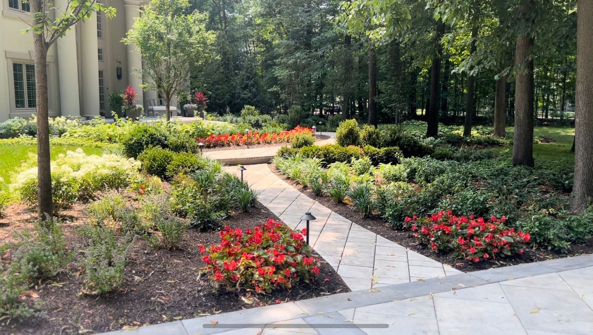A stone walkway surrounded by flowers and trees in a garden.