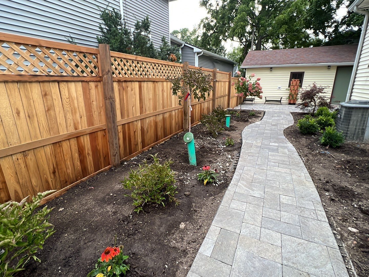 A wooden fence surrounds a brick walkway leading to a house.