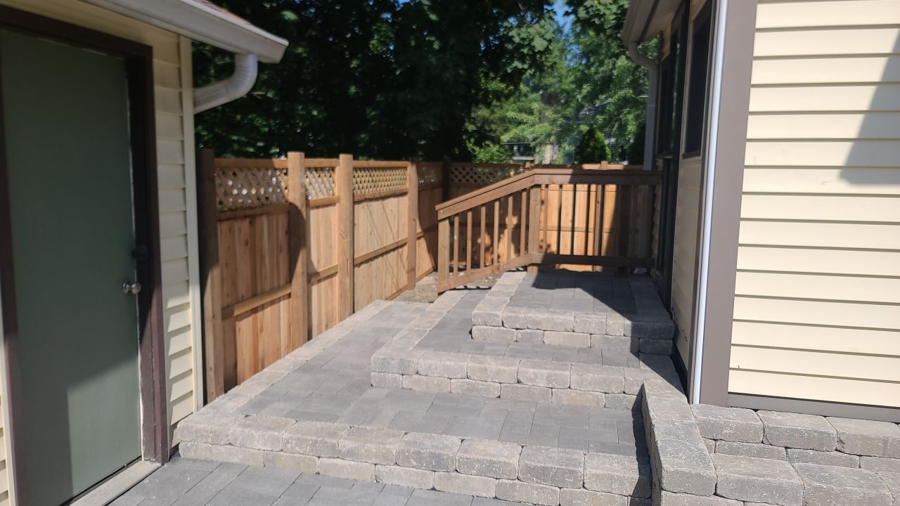 A patio with a wooden fence and stairs leading to a house.