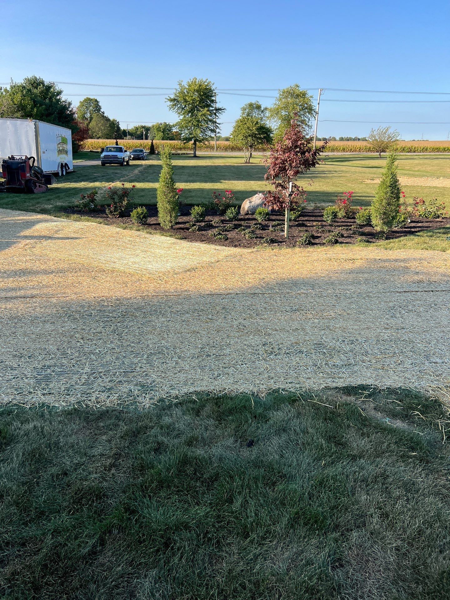 A gravel driveway leading to a field with trees and a trailer in the background.