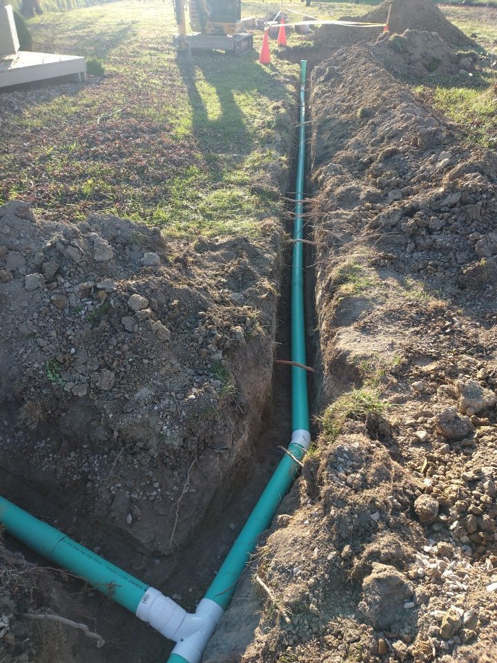 A green pipe is being installed in the dirt
