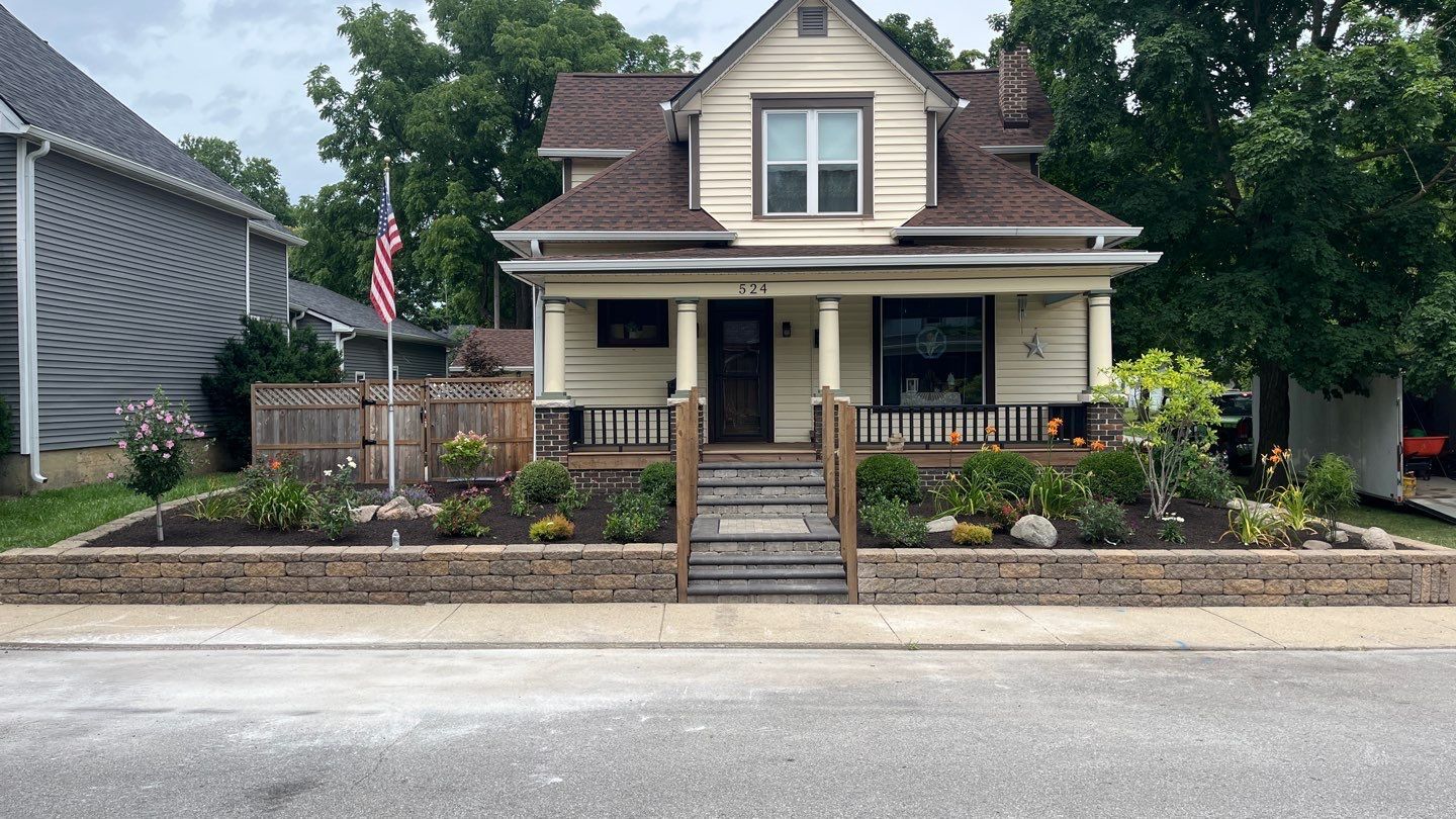 A house with a brick wall in front of it and a flag on the front porch.