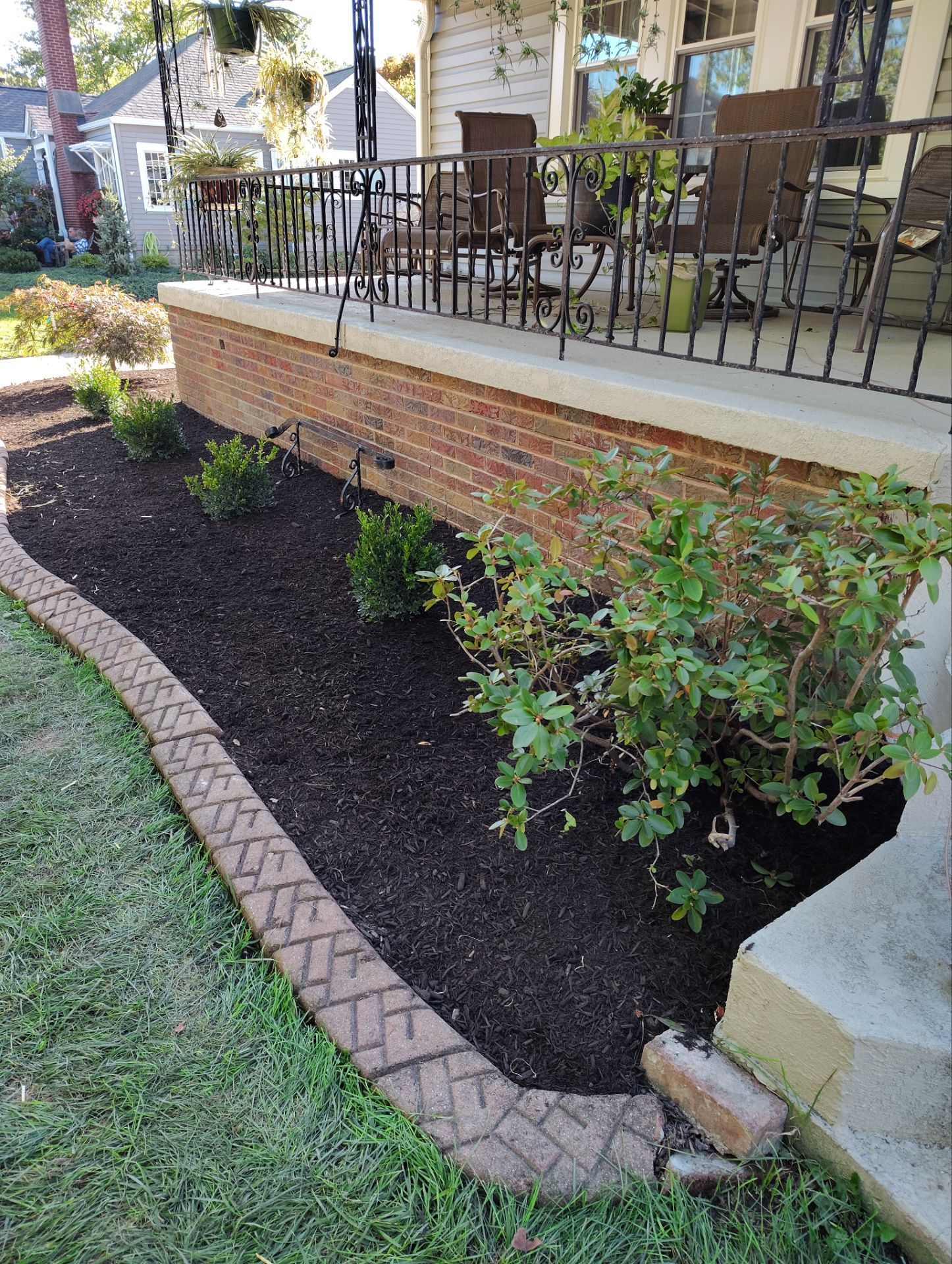 A brick house with a porch and a garden in front of it.