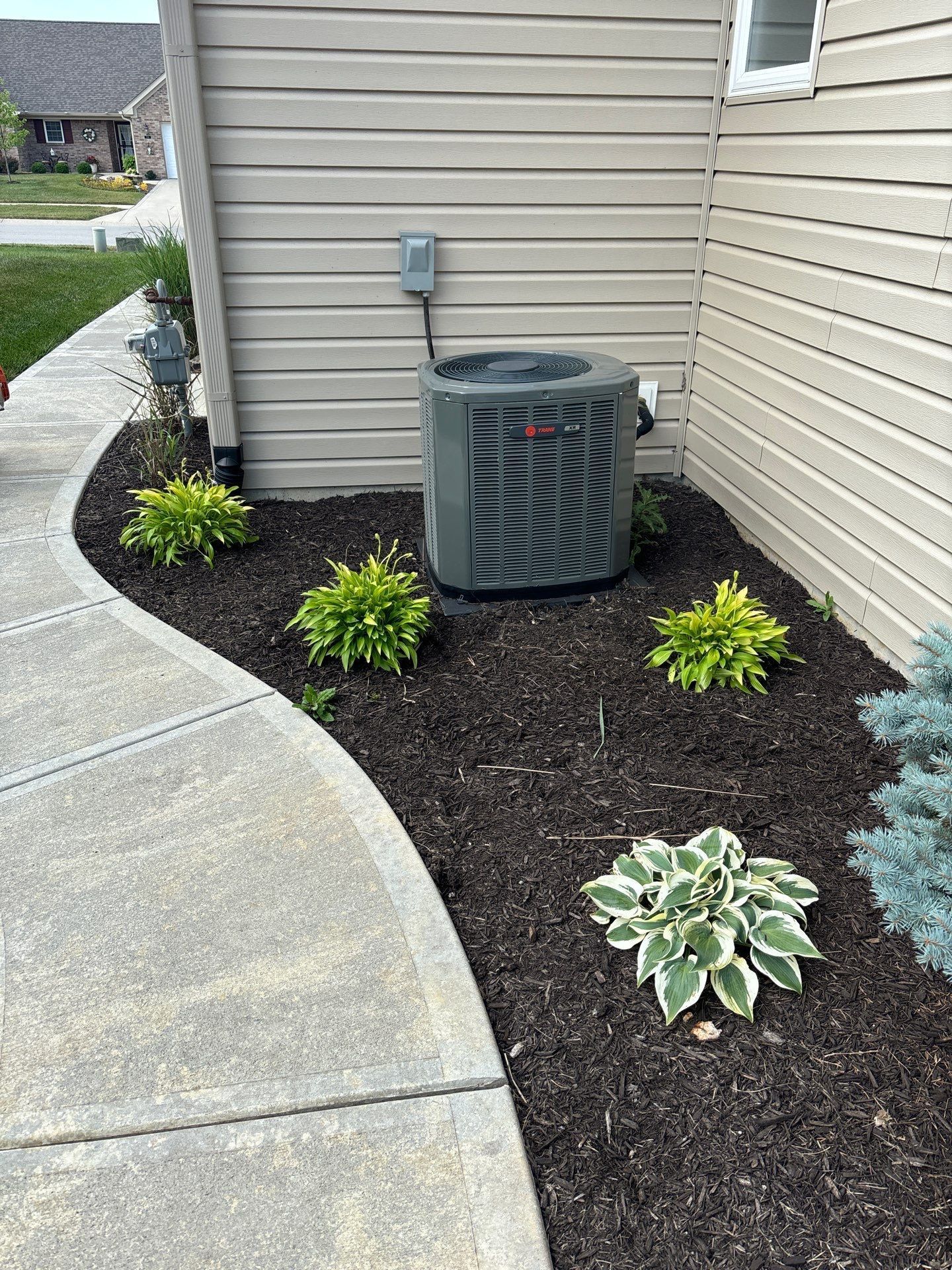 An air conditioner is sitting on the side of a house next to a sidewalk.