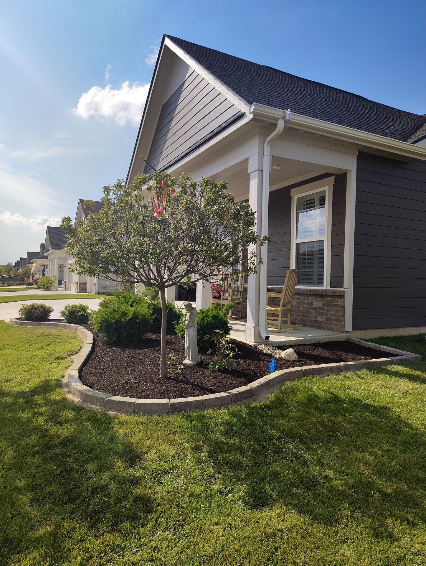 A small house with a porch and a tree in front of it.