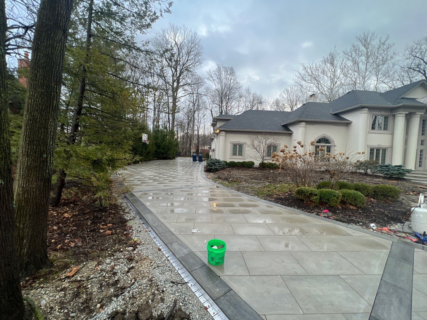 A green bucket is sitting on the sidewalk in front of a large house.