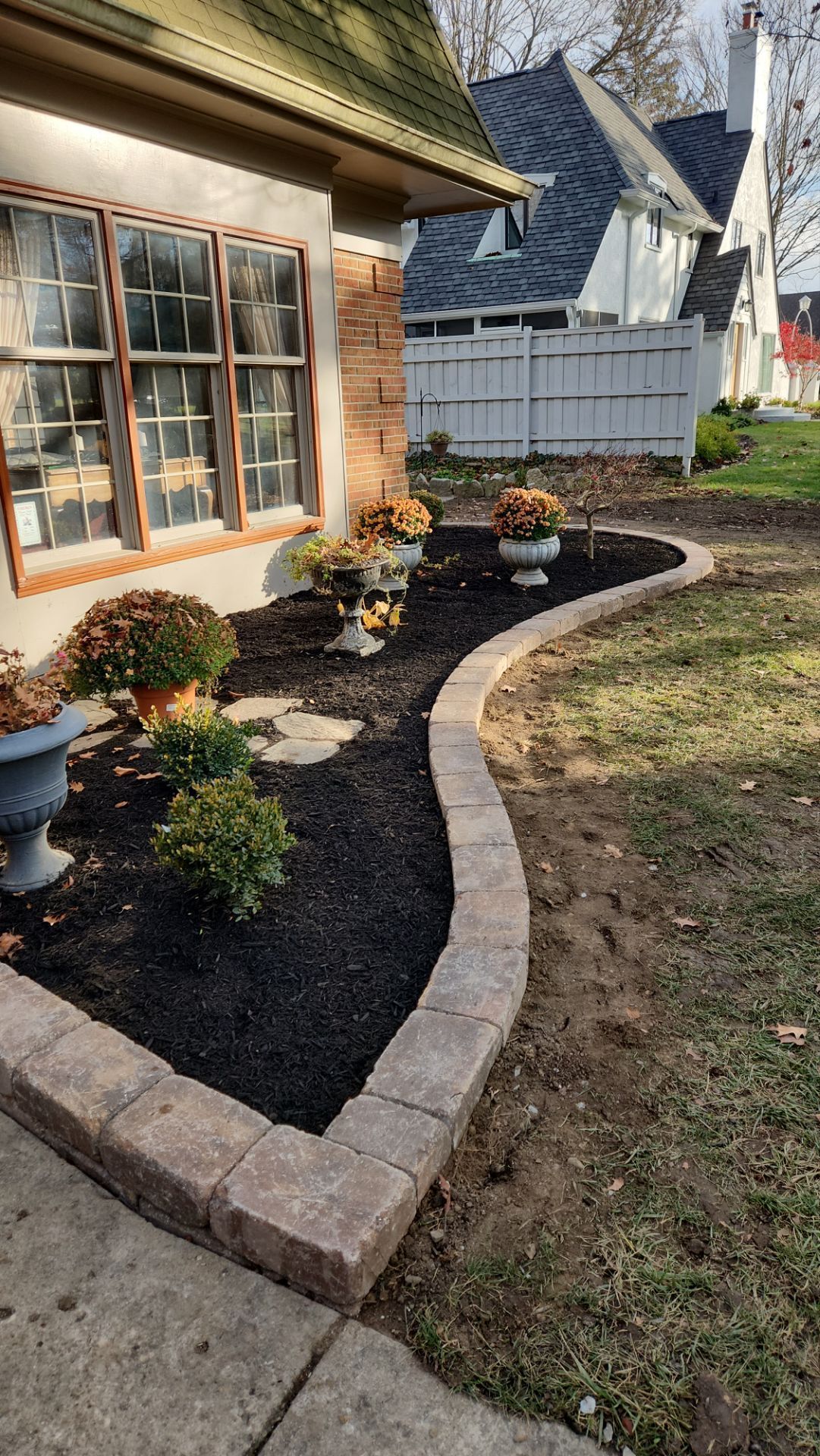 A brick walkway leading to a house with a garden in front of it.