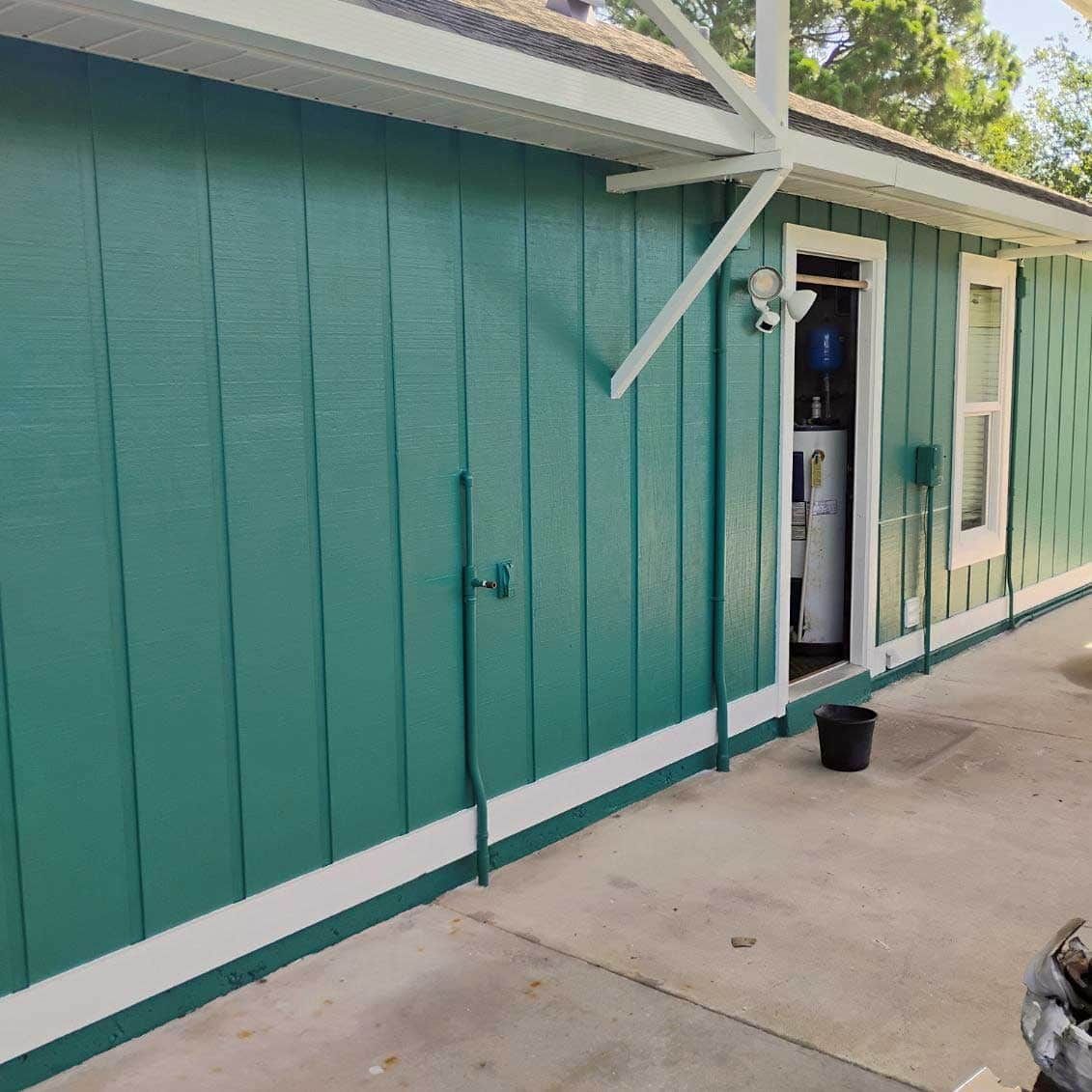 Green-painted building with white trim. Door is open to reveal a glimpse of the interior and an appliance.
