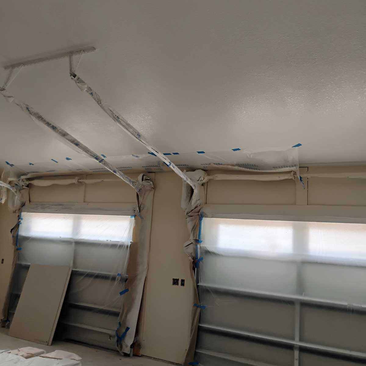 Room with ceiling and walls painted white, windows covered with plastic for protection. Construction in progress.