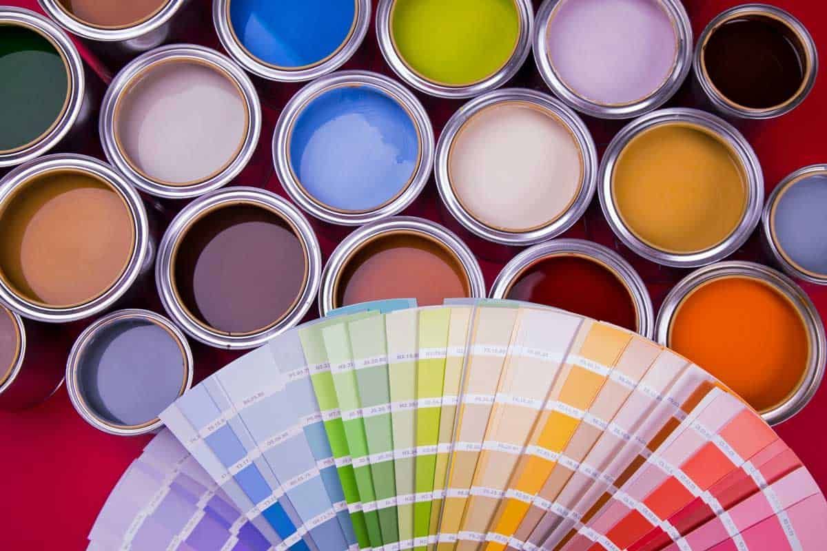 Open paint cans of various colors with a color swatch fan in front.