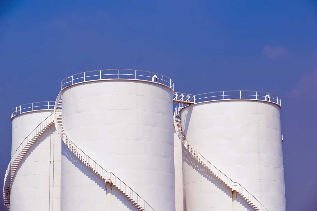 Three white cylindrical storage tanks against a blue sky, with external spiral staircases.