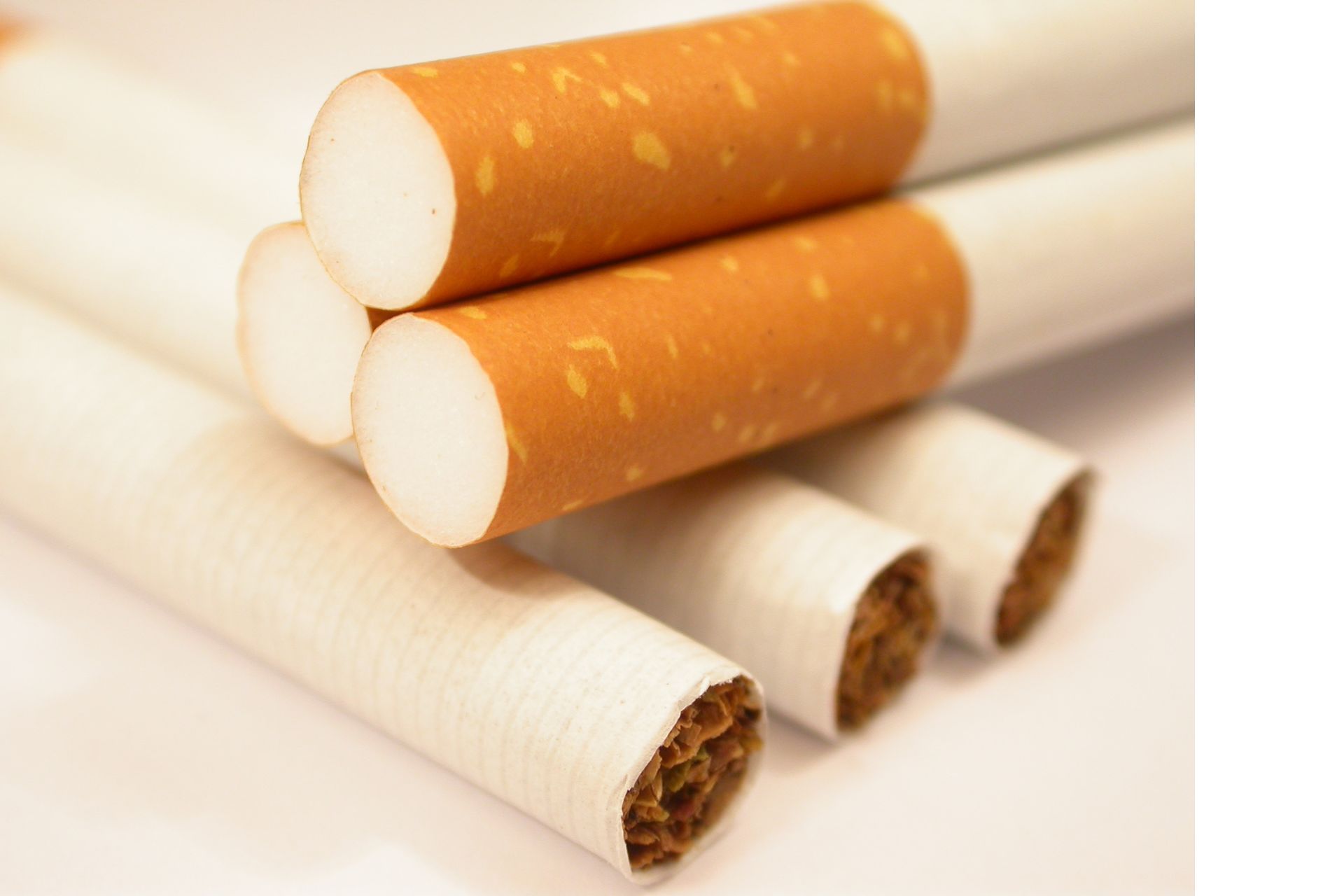 A close-up view of several unlit cigarettes with brown filters, arranged in a small pile against a white background.