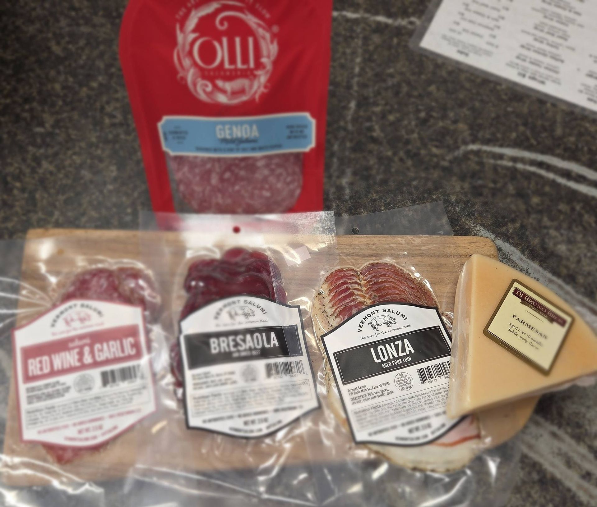 A selection of Olli and Tempesta cured meats including salami, bresaola, and lonza, plus a wedge of cheese on a board.