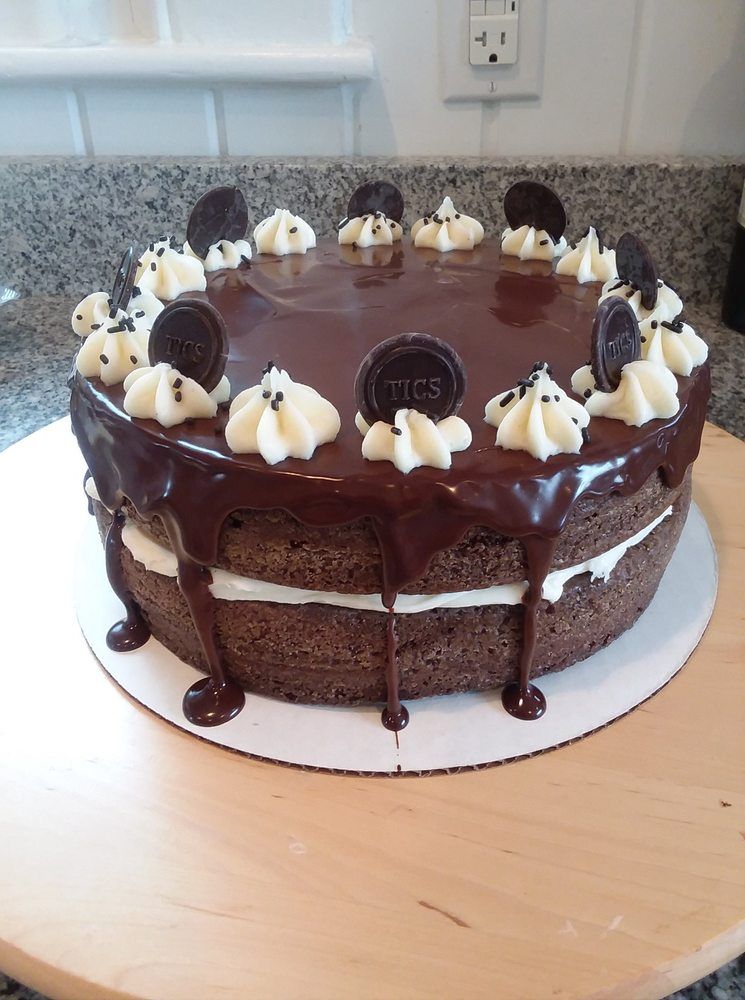 A chocolate layer cake with vanilla frosting, chocolate ganache drips, and Oreo cookie decorations.