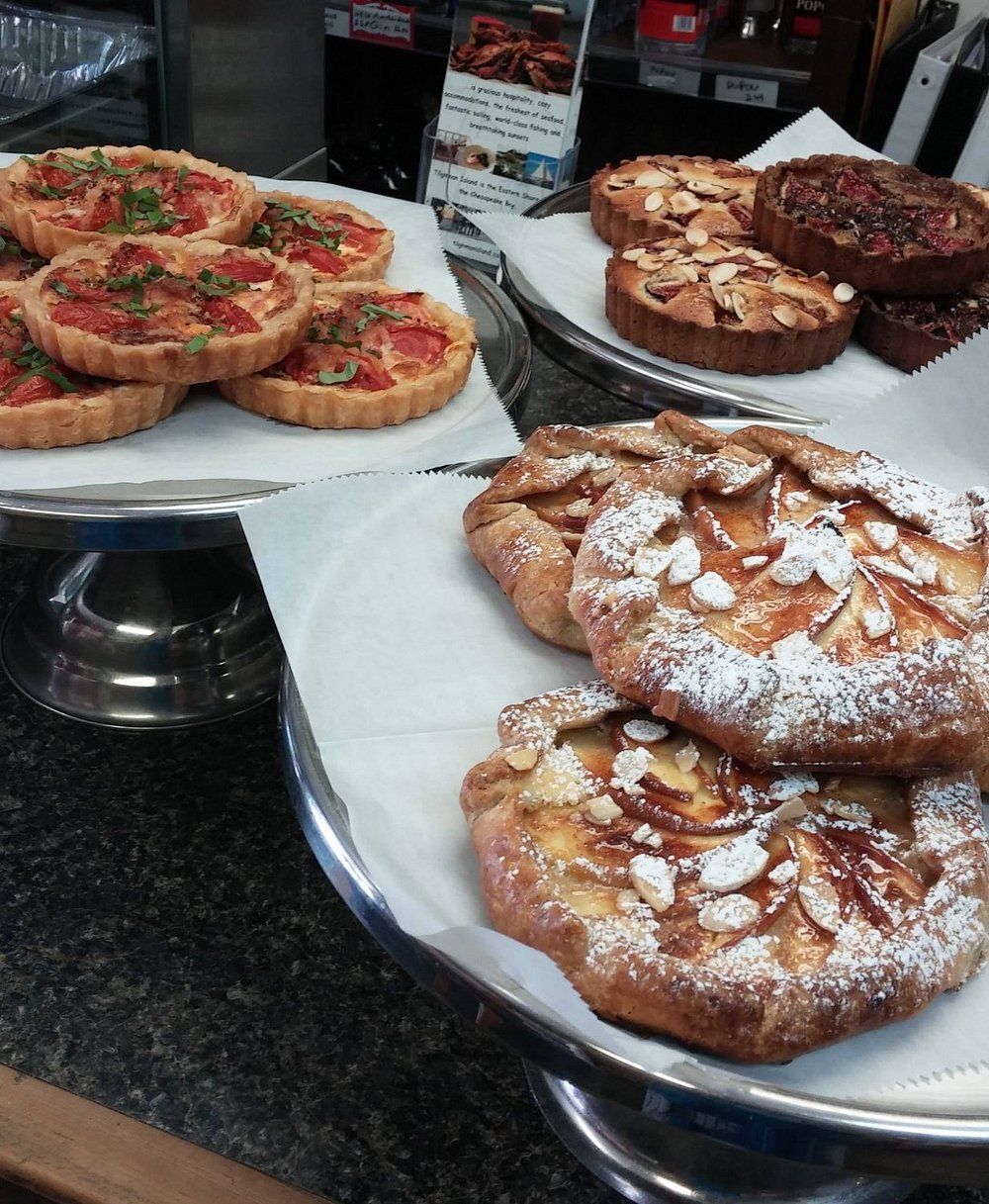 Three silver trays hold various savory tomato tarts, round chocolate desserts, and rustic fruit galettes with almonds.