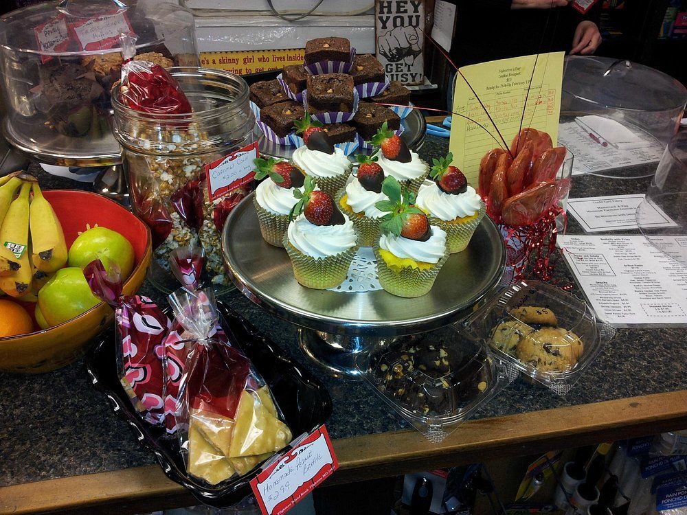 A display of assorted baked goods including cupcakes with strawberries, brownies, cookies, and fruit on a cafe counter.