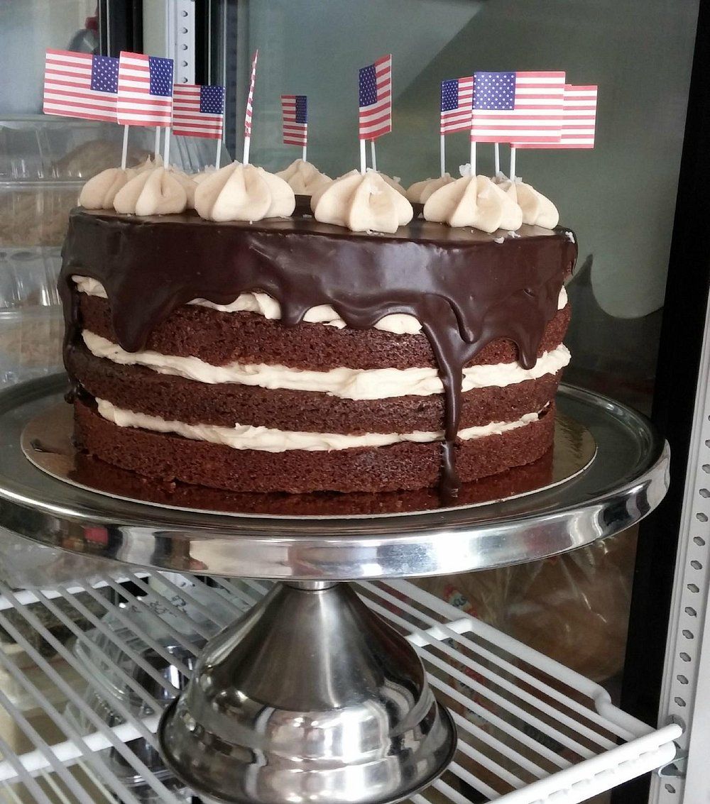A three-layer chocolate cake with frosting and chocolate ganache, topped with several small American flag picks.
