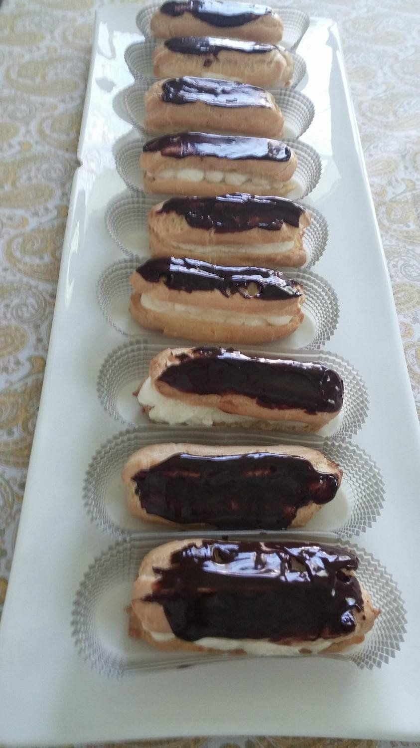 A row of nine chocolate-glazed cream-filled eclairs served on individual paper liners on a long white rectangular plate.
