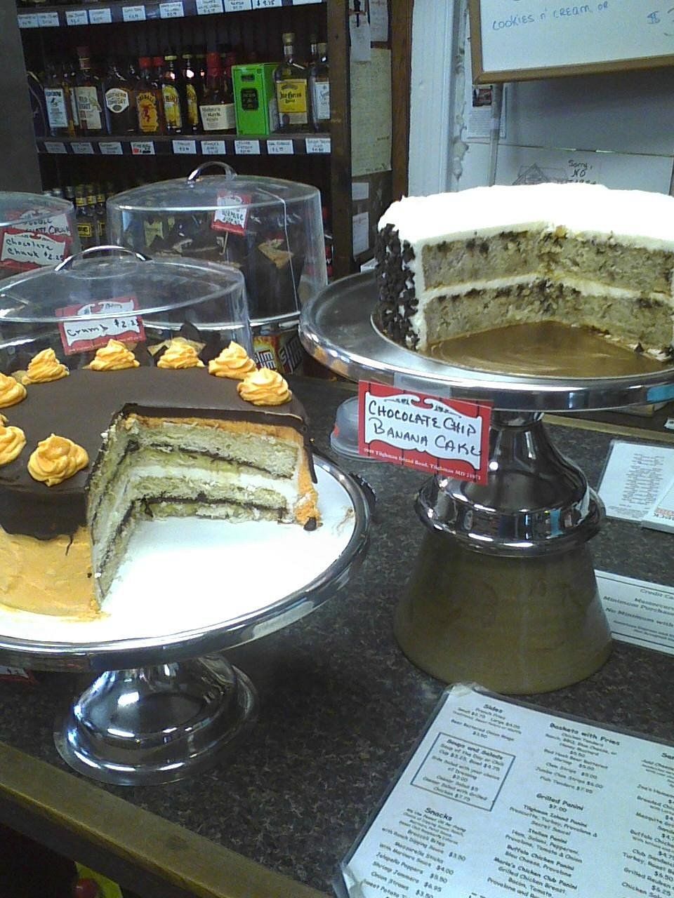 Two layer cakes on stands displayed on a shop counter, one with chocolate frosting and orange swirls, the other plain.