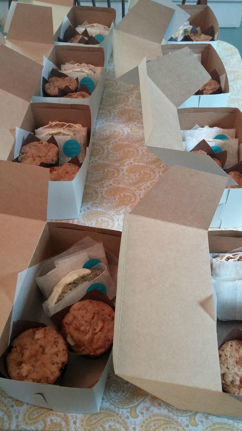 An overhead view of several open cardboard takeout boxes, each containing assorted baked goods like cookies and muffins.