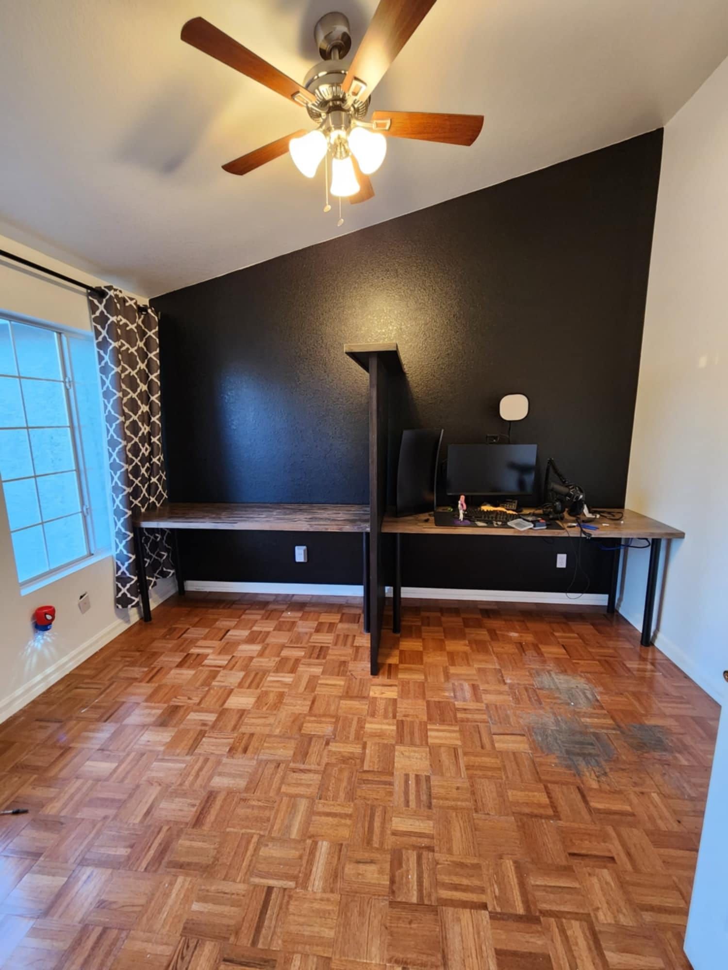 A room with two desks and a ceiling fan.