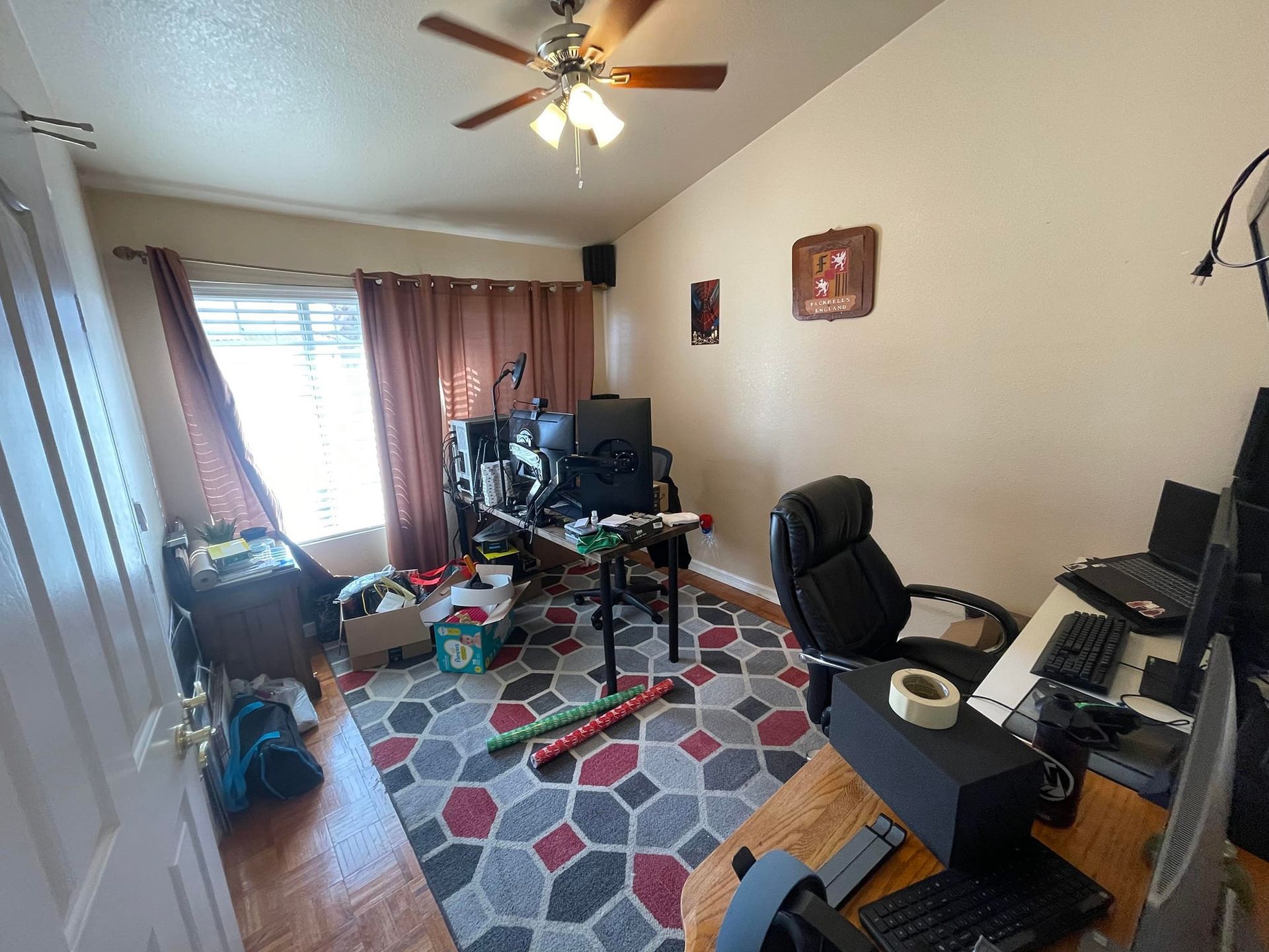 A room with a desk , chair , computer and a ceiling fan.