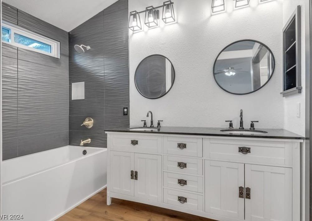 A bathroom with two sinks , two mirrors and a bathtub.