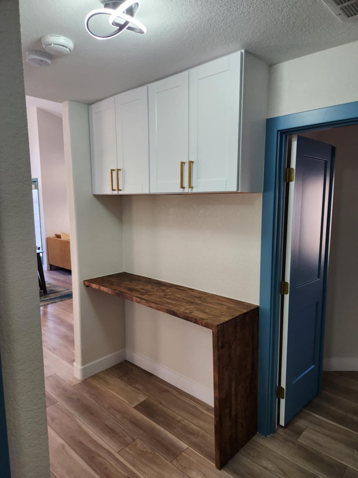 A hallway with a wooden desk and white cabinets above it.