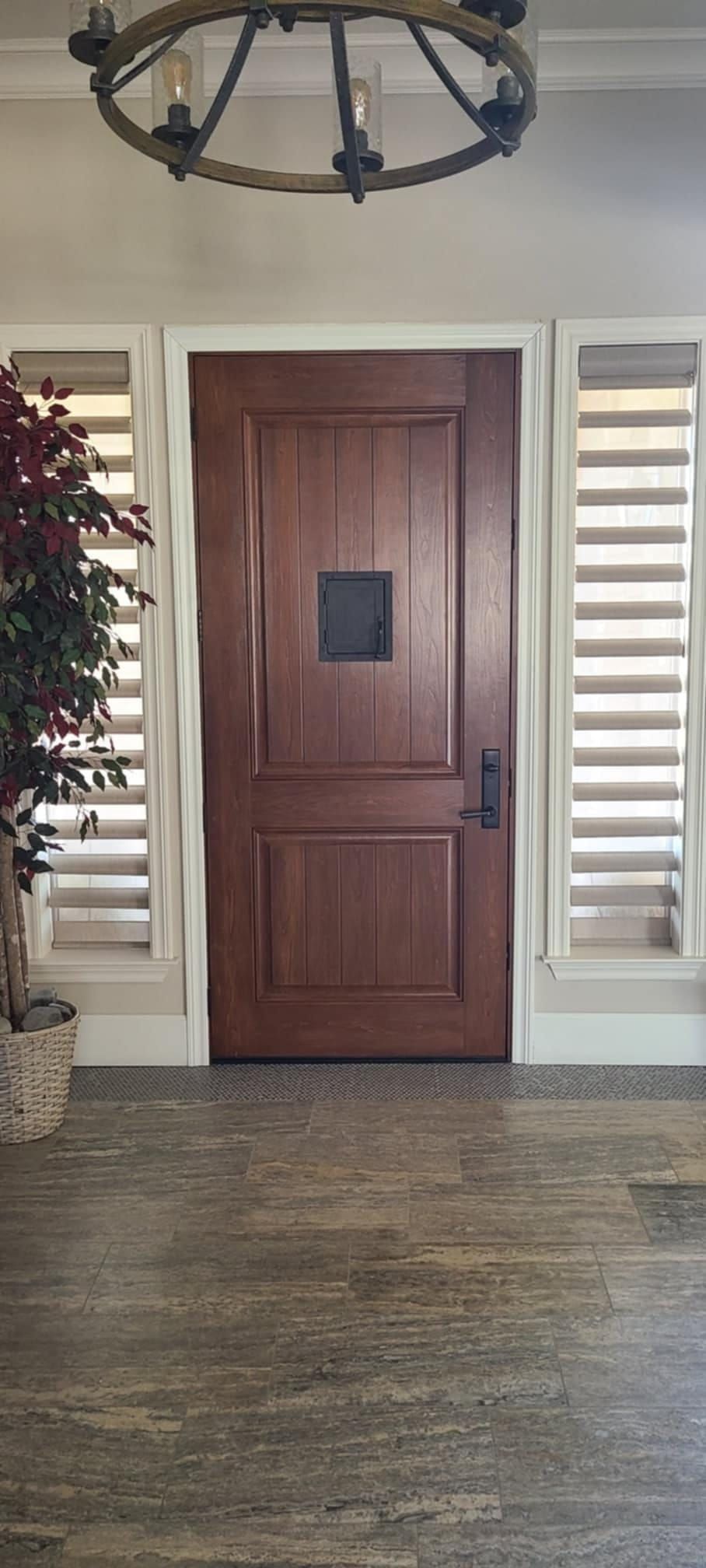 A wooden door with a window in the middle of it is in a room with shutters and a chandelier.
