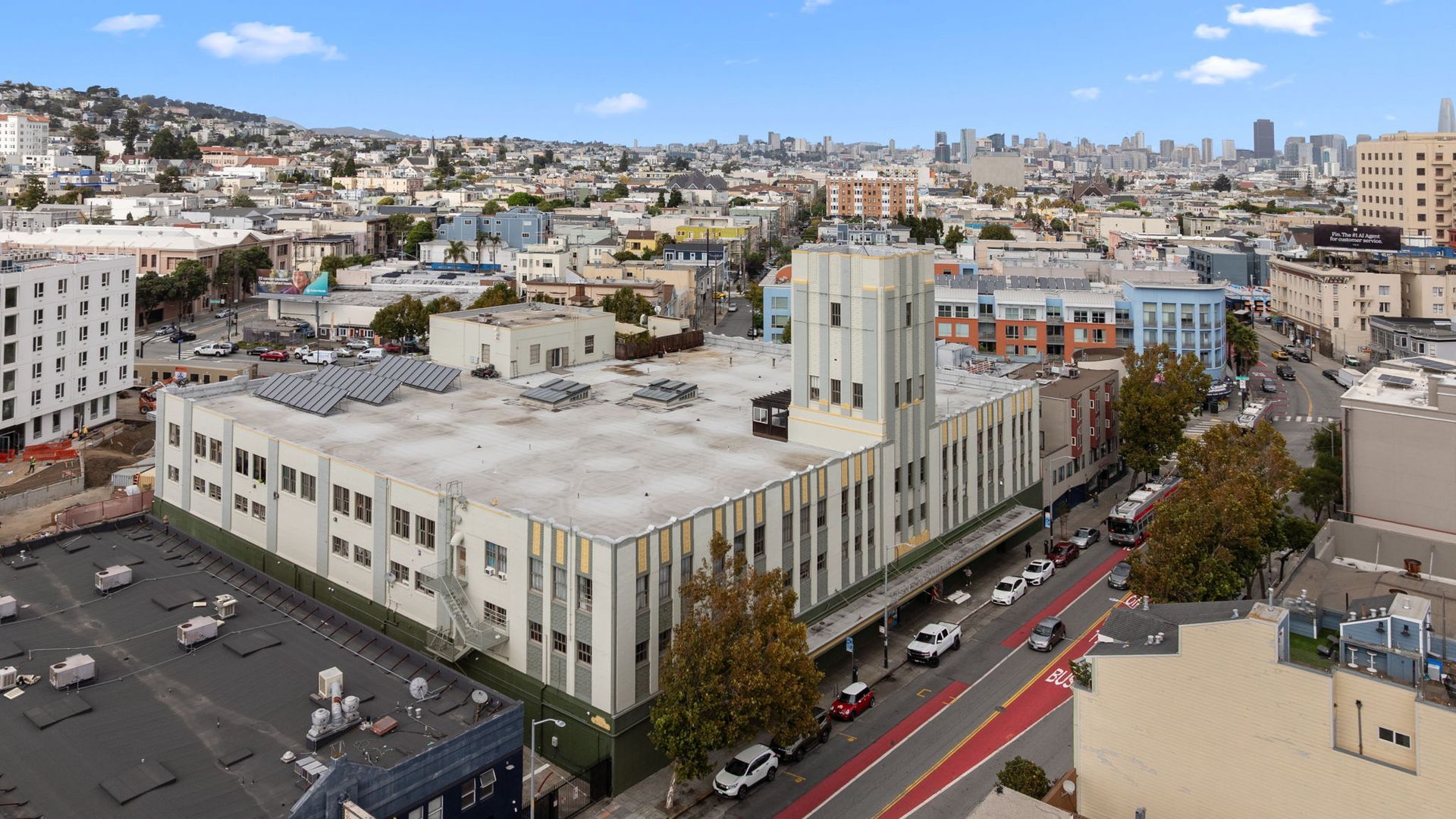Aerial view of a large, art deco style building in a city. Includes a parking lot, street, and cityscape in the background.
