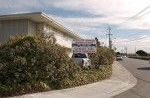 Building with a sign partially obscured by bushes, next to a street with cars and power lines.
